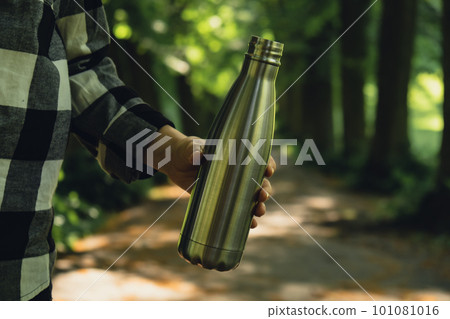 Close-up of Unrecognizable female hand holding Water bottle. Reusable steel thermo water bottle in park. Sustainable lifestyle. Plastic free zero waste free living. Go green Woman drinking water in 101081016