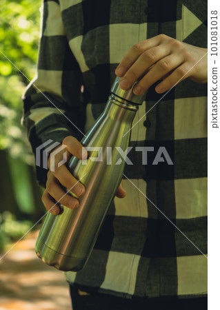 Close-up of Unrecognizable female hand holding Water bottle. Reusable steel thermo water bottle in park. Sustainable lifestyle. Plastic free zero waste free living. Go green Woman drinking water in 101081018