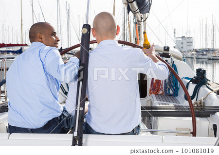 Two men in blue shirts sitting with their backs on yacht in the port 101081019