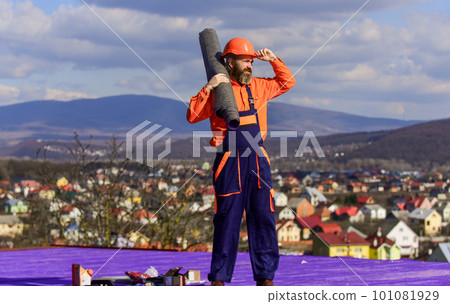 Apply plastic coatings membranes fiberglass or felt over sloped roofs before applying shingles. Roofer repair roof. Roof installation. Man hard hat work outdoor landscape background. Building house 101081929