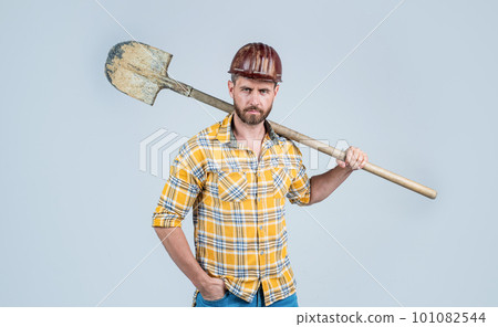 handsome man laborer in construction safety helmet and checkered shirt on building site with shovel, industry 101082544