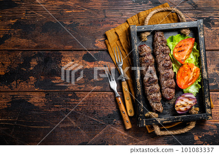 Traditional middle east kefta or kofta kebab, ground beef and lamb meat grilled on skewers served with tomato, salad and onion. Wooden background. Top view. Copy space Traditional middle east kefta or kofta kebab, ground beef and lamb meat grilled on skewers served with tomato, salad and onion. Wooden background. Top view. Copy space 101083337