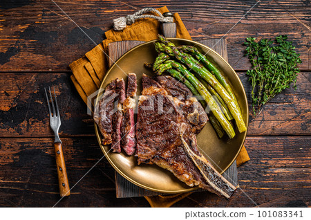 Sliced Grilled Cowboy or rib eye with bone beef steak, roasted asparagus in a plate. Wooden background. Top view 101083341