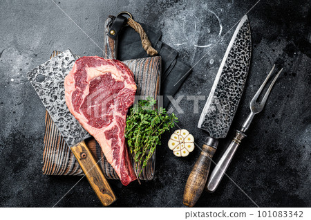 Dry aged Tomahawk rib eye steak, raw beef meat on butcher table. Black background. Top view 101083342