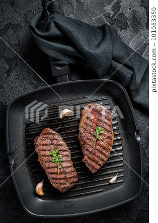 Grilled Top Blade or flat iron roast beef meat steaks on a skillet. Black background. Top View 101083350