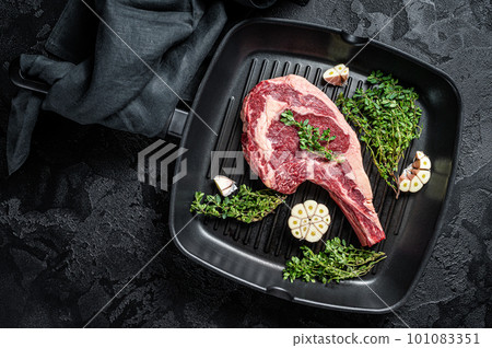 Ready for cooking Raw cowboy or rib eye steak in a grill skillet. Black background. Top view 101083351