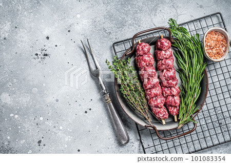 Raw Turkish Urfa kebab decorated with herbs, spices and meat fork. Gray background. Top view. Copy space Raw Turkish Urfa kebab decorated with herbs, spices and meat fork. Gray background. Top view. Copy space 101083354