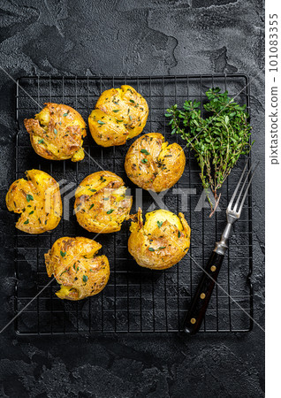 Crushed, smashed potatoes baked with rosemary and thyme. Black background. Top view Crushed, smashed potatoes baked with rosemary and thyme. Black background. Top view 101083355