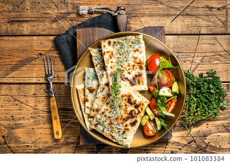 Gozleme flatbread with greens and vegetable salad on garnish. Wooden background. Top view 101083384
