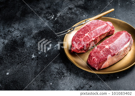 Raw Shoulder Top Blade beef meat steaks on a plate. Black background. Top View. Copy space Raw Shoulder Top Blade beef meat steaks on a plate. Black background. Top View. Copy space 101083402