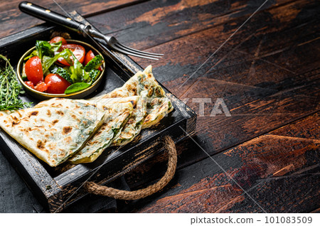 Baked Gozleme flatbread with greens in a box with vegetable salad. Wooden background. Top view. Copy space Baked Gozleme flatbread with greens in a box with vegetable salad. Wooden background. Top view. Copy space 101083509