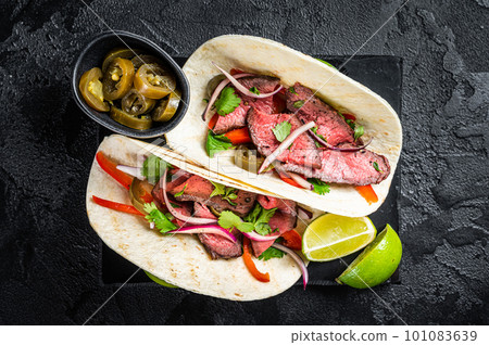 Mexican Steak Tacos with beef meat, cilantro, green sauce, jalapenos and onion. Black background. top view Mexican Steak Tacos with beef meat, cilantro, green sauce, jalapenos and onion. Black background. top view 101083639