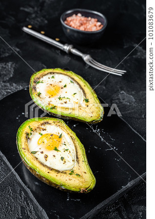 Eggs baked in avocado with herbs and spices. Black background. Top view Eggs baked in avocado with herbs and spices. Black background. Top view 101083679