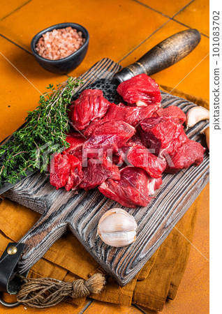 Raw beef meat chopped in cubes on wooden cutting board for cooking stew. Orange background. Top view Raw beef meat chopped in cubes on wooden cutting board for cooking stew. Orange background. Top view 101083702