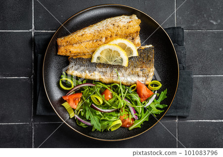 Roasted sea bass fillet with salad, Branzino fish. Black background. Top view Roasted sea bass fillet with salad, Branzino fish. Black background. Top view 101083796