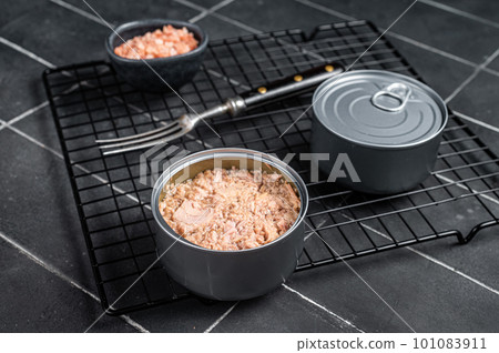 Canned tuna fillet meat in olive oil in a tin. Black background. Top view 101083911