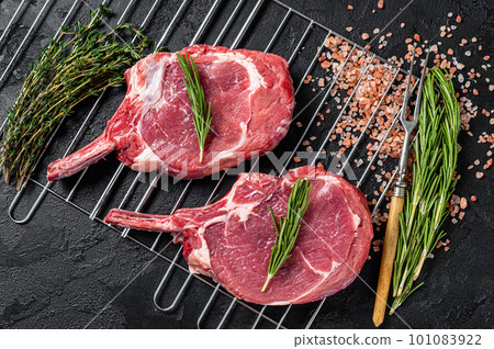 Fresh Raw Tomahawk rib eye beef steaks on grill. Black background. Top view 101083922