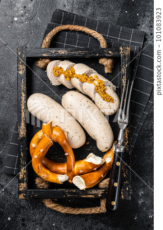 Bavarian meal with white sausages and sweet mustard in wooden tray with Pretzel. Black background. Top view 101083923