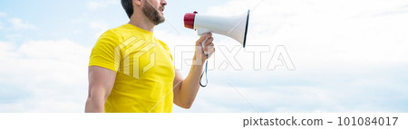 cropped view of man in yellow shirt shout in loudspeaker on sky background 101084017
