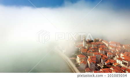 Mysterious drone view of the ancient city of Budva during heavy cloud cover. Old medieval city with red roofs in Montenegro on the sunset. 101085034