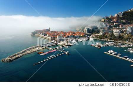 Mysterious drone view of the ancient city of Budva during heavy cloud cover. Old medieval city with red roofs in Montenegro on the sunset. Mysterious drone view of the ancient city of Budva during heavy cloud cover. Old medieval city with red roofs in Montenegro on the sunset. 101085038