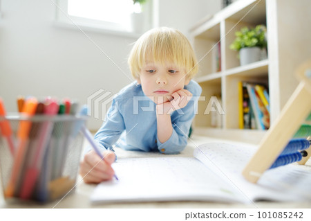 Elementary student boy doing homework on floor at home. Child learning to count, solves arithmetic examples in workbook. Math tutorial. Preparing preschooler baby for school. 101085242