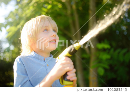 Funny little boy watering plants and playing with garden hose with sprinkler in sunny backyard. Preschooler child having fun with spray of water. Funny little boy watering plants and playing with garden hose with sprinkler in sunny backyard. Preschooler child having fun with spray of water. 101085243