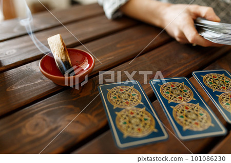 Fortune teller with tarot cards on table near burning candle.Tarot cards spread on table with magic herbs and palo santo aroma sticks. Forecasting concept Fortune teller with tarot cards on table near burning candle.Tarot cards spread on table with magic herbs and palo santo aroma sticks. Forecasting concept 101086230