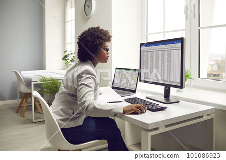 Woman accountant sitting at her desk, using computers, and working with business spreadsheets 101086923