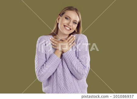 Smiling blondy woman in purple sweater keeping hands at chest or heart on khaki background. 101086937