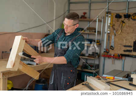 The carpenter shakes off sawdust from a wooden product. The carpenter shakes off sawdust from a wooden product. 101086945