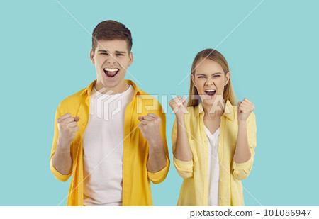 Overjoyed young Caucasian man and woman raise their fists and shout Yes, stands in turquoise studio 101086947