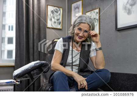Grey-haired woman sitting on couch in the tattoo salon 101086976