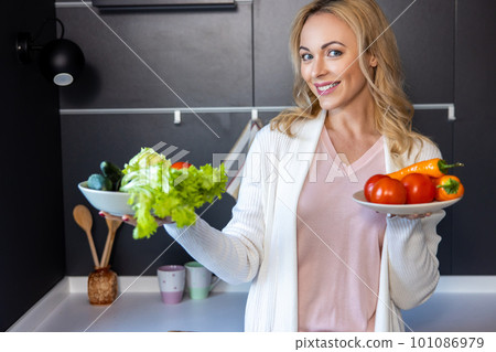 Cheerful young housewife showing salad ingredients before the camera Cheerful young housewife showing salad ingredients before the camera 101086979