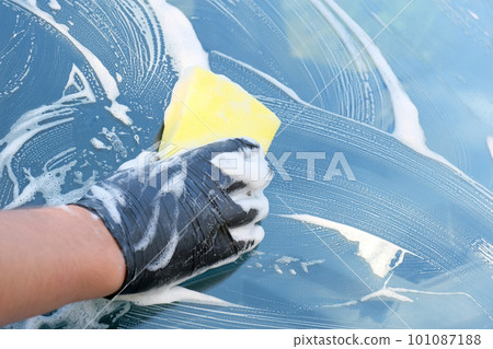 Car wash with soap. The hand of a man in a black glove wipes the windshield with a sponge 101087188
