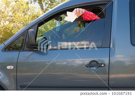 Mans hand throws trash from the car window on the road. Side view. Mans hand throws trash from the car window on the road. Side view. 101087191