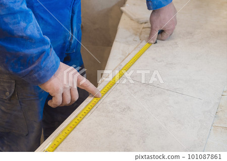 Builder with a measuring tape measures the tiles. Construction repair work Builder with a measuring tape measures the tiles. Construction repair work 101087861