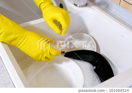 Hands in protective rubber gloves washing dirty dishes in the kitchen Hands in protective rubber gloves washing dirty dishes in the kitchen 101088524