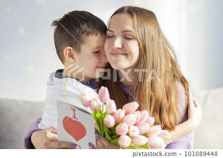 Boy congratulating his mom and giving her flowers tulips and greeting card Boy congratulating his mom and giving her flowers tulips and greeting card 101089448