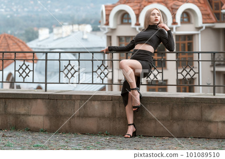 Sexy blonde model in tight black clothes and heels poses on urban architecture background. Sexy blonde model in tight black clothes and heels poses on urban architecture background. 101089510