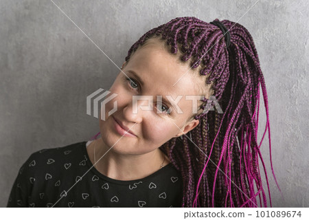 Attractive young woman with many pigtails gathered in tail looks into the camera. Portrait of stylish girl with pink dreadlocks. 101089674