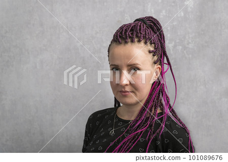 Portrait of serious young caucasian woman with pink artificial dreadlocks on gray background. Middle aged woman 101089676