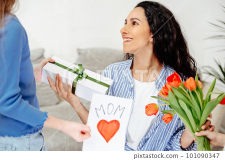 Mom is happy to receive an unexpected gift from her children. Children give their mother a bouquet of tulips, a handmade card and a surprise box. Mom is happy to receive an unexpected gift from her children. Children give their mother a bouquet of tulips, a handmade card and a surprise box. 101090347
