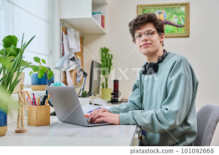 Young male college student sitting at desk at home using laptop Young male college student sitting at desk at home using laptop 101092668