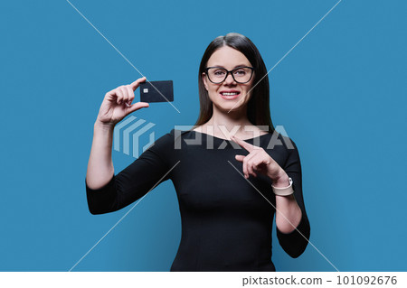 Young woman holding credit card in her hands on blue background Young woman holding credit card in her hands on blue background 101092676