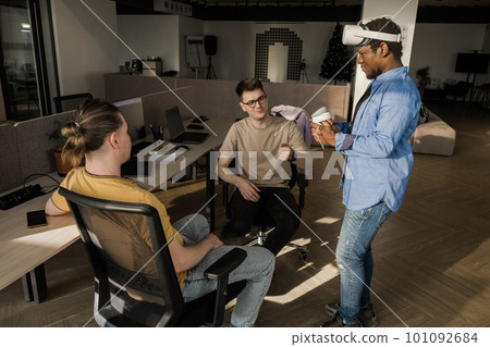 IT Development Team Working on VR Project. Man wearing VR headset, playing and touching something in the virtual world. Diverse men programmers using VR technologies and computer to create video game. 101092684