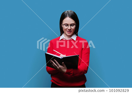 Young woman writes in business diary, on blue studio background. Young woman writes in business diary, on blue studio background. 101092829