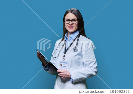 Young friendly woman doctor with clipboard on blue studio background Young friendly woman doctor with clipboard on blue studio background 101092831