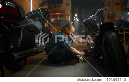 Mature man biker repairing motorcycle in garage at evening 101093240
