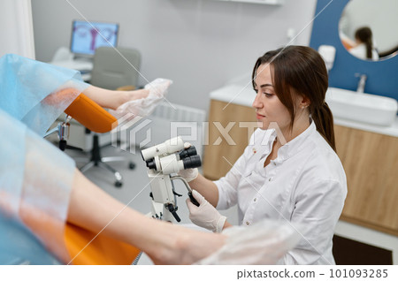 Gynecologist examining patient on chair with gynecological microscope 101093285